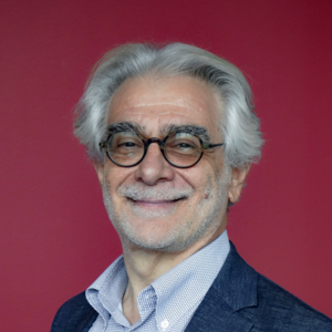 Professor Vettori smiles at the camera, wearing circular black-rimmed glasses. 