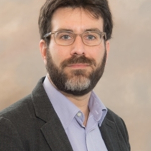 Daniel Leisawitz, fully bearded with glasses, lavender dress shirt and grey sports coat