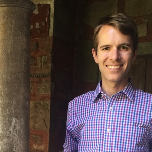 James Coleman wearing a blue and red plaid shirt standing in front of a old building