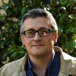 Prof has glasses, wearing a tan coat, blue dress shirt