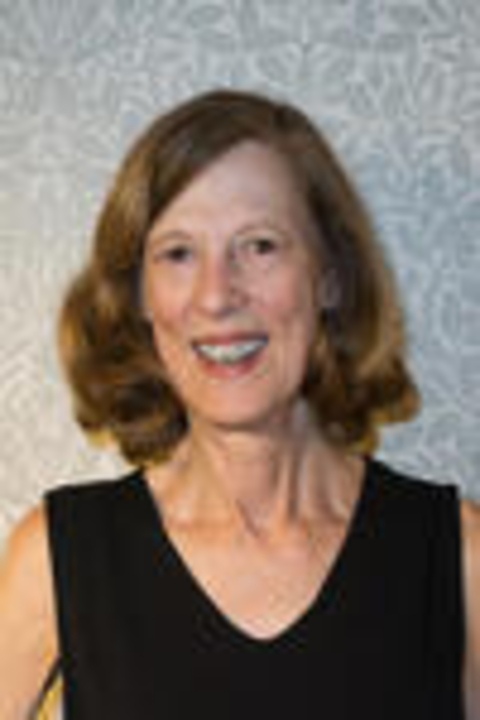A portrait of Professor Millicent Marcus, standing in front of a wallpapered wall and wearing a black dress. She is smiling at the camera.