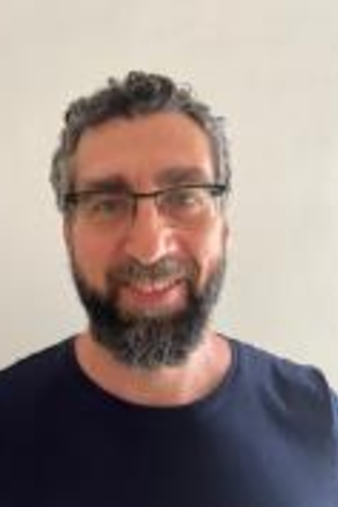 Andrea Moudarres fully bearded, greyish hair wearing a blue shirt
