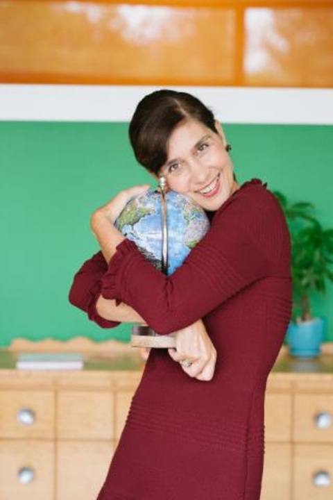 Christina Ball with short brown hair, wearing a burgundy dress and hugging a globe.
