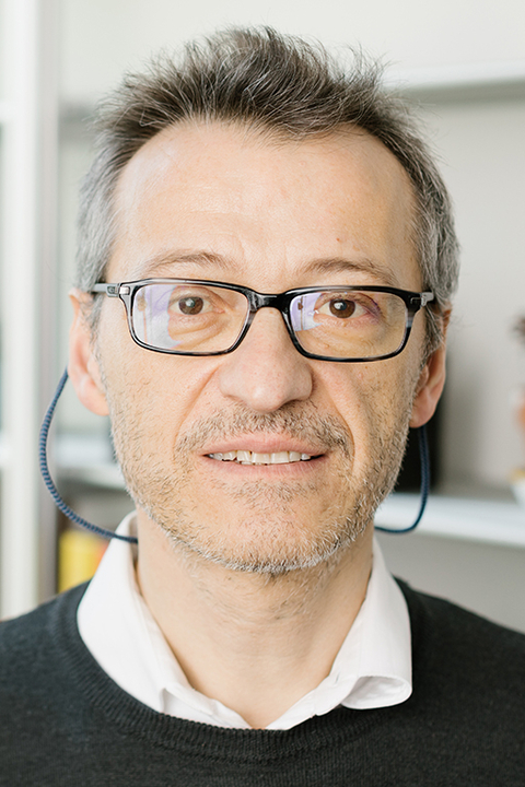 Massimo Scalabrini, wearing black-rimmed glasses and standing in an office